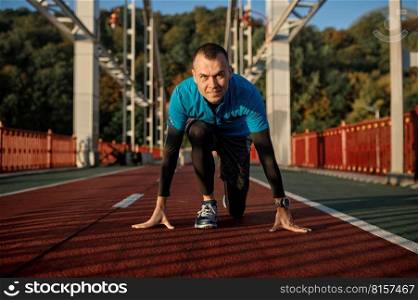 Portrait of adult speed runner in starting position ready for running on sports track. Adult speed runner in starting position ready for running on sports track