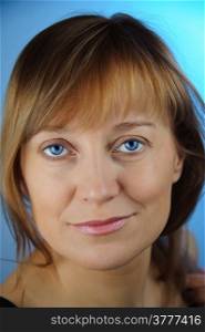 Portrait of adult woman with a smirk. Look at the camera. Blue background. Closeup.