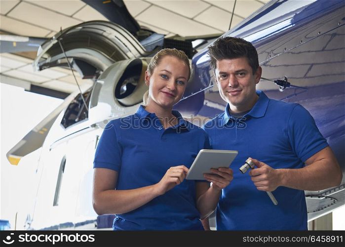 Portrait Of Aero Engineer And Apprentice Working On Helicopter In Hangar Looking At Digital Tablet