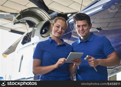 Portrait Of Aero Engineer And Apprentice Working On Helicopter In Hangar Looking At Digital Tablet