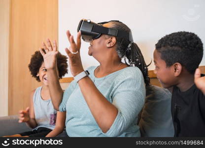 Portrait of African American grandmother and grandchildren playing together with VR glasses at home. Family and technology concept.