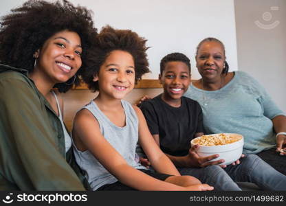 Portrait of African American grandmother, mother and children looking at camera and smiling while sitting on sofa at home. Family and lifestyle concept.