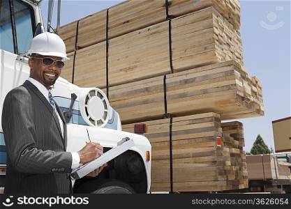 Portrait of African American male contractor writing notes while standing by logging truck