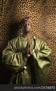 Portrait of African- American mid-adult man in prayer wearing traditional African clothing.