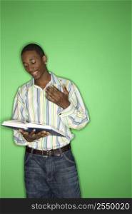 Portrait of African-American teen boy reading book standing in front of green background.