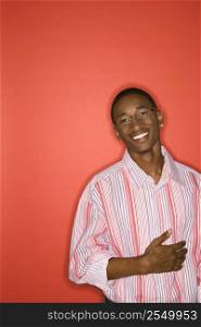 Portrait of African-American teen boy smiling with hand on abdomen standing against red background.