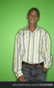 Portrait of African-American teen boy with one hand in pocket standing against green background.