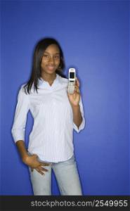 Portrait of African-American teen girl holding cellphone and hand in pocket standing against blue background.