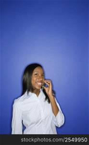 Portrait of African-American teen girl smiling and holding cellphone standing against blue background.