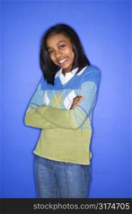 Portrait of African-American teen girl with arms crossed standing against blue background.