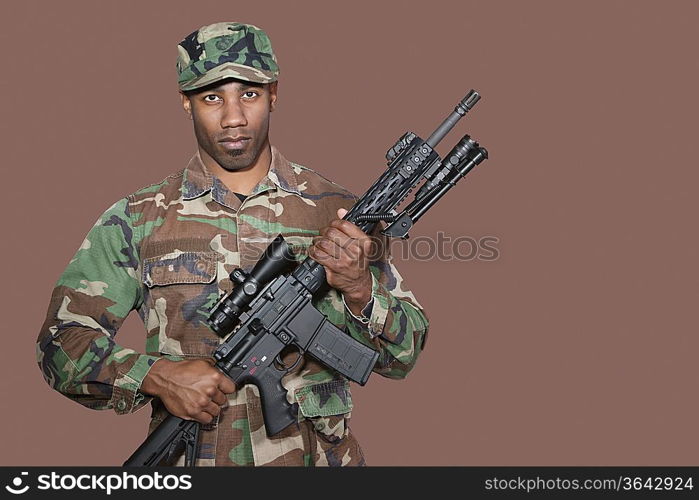 Portrait of African American US Marine Corps soldier holding M4 assault rifle over brown background