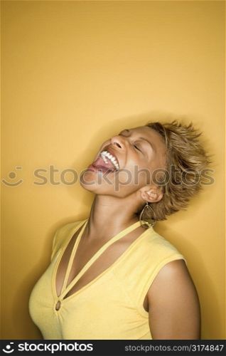 Portrait of African-American young adult woman laughing with head back on yellow background.