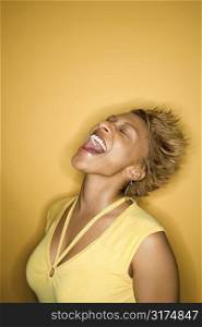 Portrait of African-American young adult woman laughing with head back on yellow background.