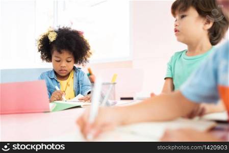 Portrait of African black girl drawing at the desk in the preschool. Diversity Little Kid drawing and colouring in the room at Kindergarten. Children Back to school.