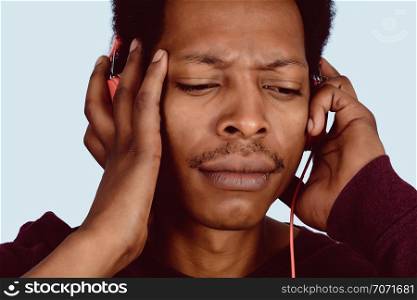 Portrait of Afro American man listening music with red headphones on studio.