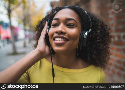 Portrait of Afro american woman smiling and listening to music with headphones in the street. Outdoors.