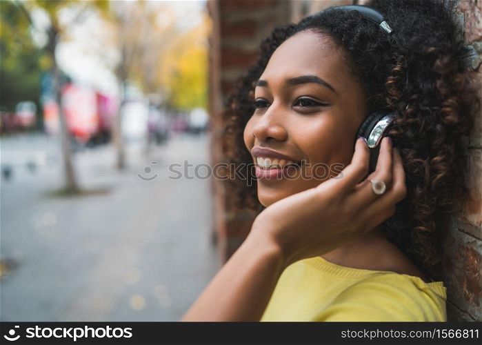 Portrait of Afro american woman smiling and listening to music with headphones in the street. Outdoors.