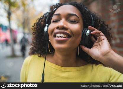 Portrait of Afro american woman smiling and listening to music with headphones in the street. Outdoors.