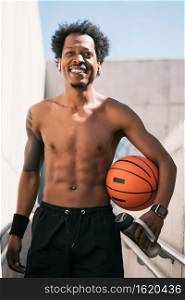 Portrait of afro athlete man holding a basketball ball and relaxing after training outdoors. Sport and healthy lifestyle.