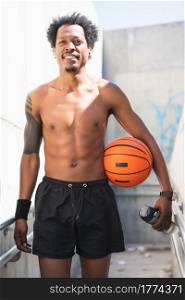 Portrait of afro athlete man holding a basketball ball and relaxing after training outdoors. Sport and healthy lifestyle.. Afro athlete man holding a basketball ball outdoors.