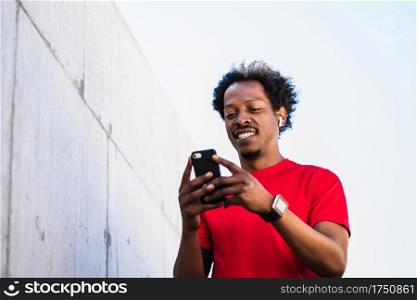 Portrait of afro athlete man using his mobile phone and relaxing after work out outdoors. Sport and healthy lifestyle.