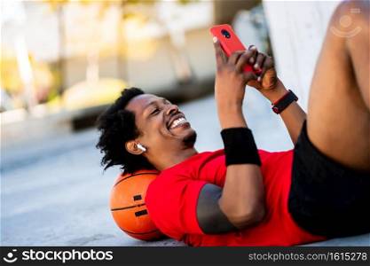 Portrait of afro athlete man using his mobile phone while laying on floor after training outdoors. Sport and healthy lifestyle.