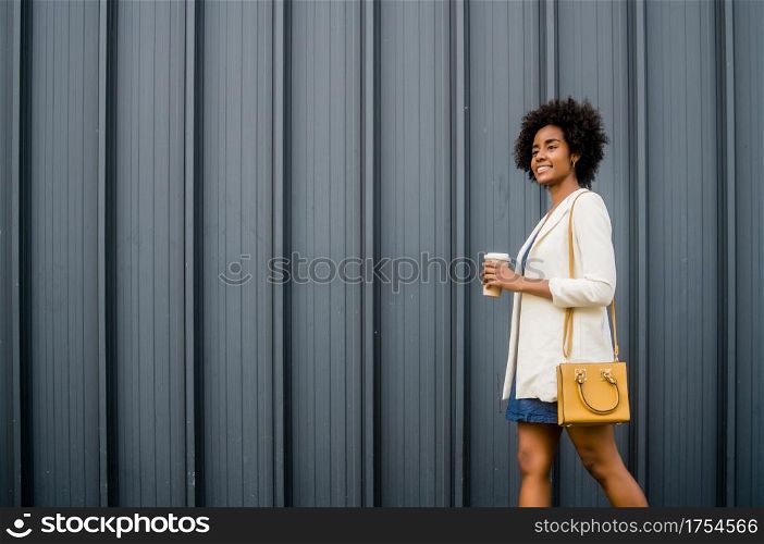 Portrait of afro business woman holding a cup of coffee while walking outdoors on the street. Business and urban concept.