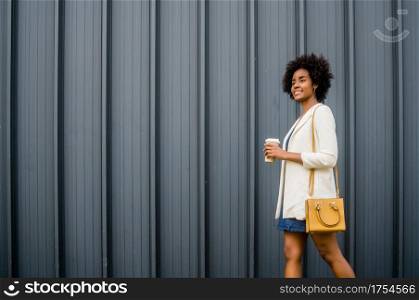 Portrait of afro business woman holding a cup of coffee while walking outdoors on the street. Business and urban concept.