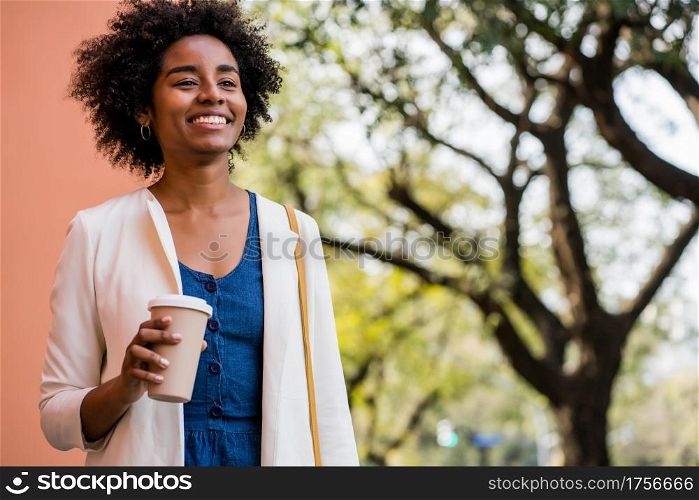 Portrait of afro business woman smiling and holding a cup of coffee while standing outdoors on the street. Business and urban concept.