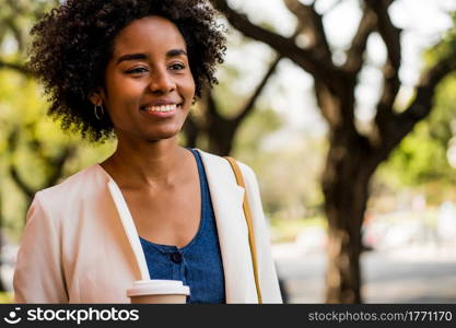 Portrait of afro business woman smiling and holding a cup of coffee while standing outdoors on the street. Business and urban concept.