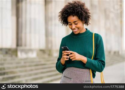 Portrait of afro business woman using her mobile phone while standing outdoors at the street. Business and urban concept.