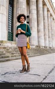 Portrait of afro businesswoman holding a cup of coffee while walking outdoors at the street. Business and urban concept.
