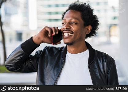 Portrait of afro man talking on the phone while walking standing outdoors on the street. Urban concept.  
