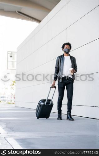 Portrait of afro tourist man carrying suitcase and holding a cup of coffee while walking outdoors on the street. Tourism concept.. Tourist man carrying suitcase while walking outdoors.