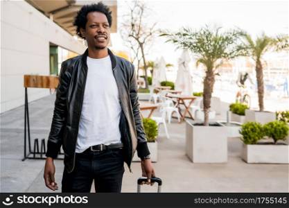 Portrait of afro tourist man carrying suitcase while walking outdoors on the street. Tourism concept.