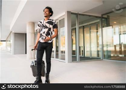 Portrait of afro tourist man carrying suitcase while walking outdoors on the street. Tourism concept.