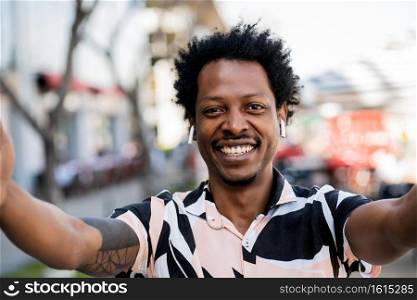 Portrait of afro tourist man taking a selfie while standing outdoors on the street. Urban and lifestyle concept.