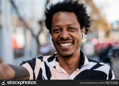 Portrait of afro tourist man taking a selfie while standing outdoors on the street. Urban and lifestyle concept.