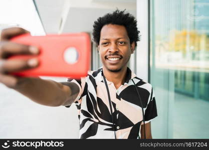 Portrait of afro tourist man taking a selfie with phone outdoors on the street. Tourism concept.