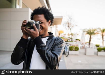 Portrait of afro tourist man taking photographs with camera while walking outdoors on the street. Tourism concept.