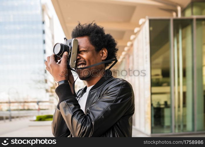 Portrait of afro tourist man taking photographs with camera while walking outdoors on the street. Tourism concept.