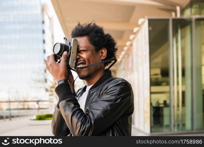Portrait of afro tourist man taking photographs with camera while walking outdoors on the street. Tourism concept.