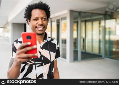 Portrait of afro tourist man using his mobile phone while walking outdoors on the street. Tourism concept.
