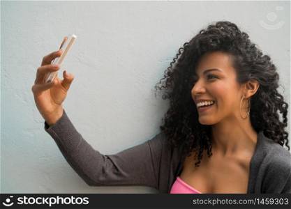 Portrait of afro woman taking selfies with her mophile phone against grey wall. Technology concept.