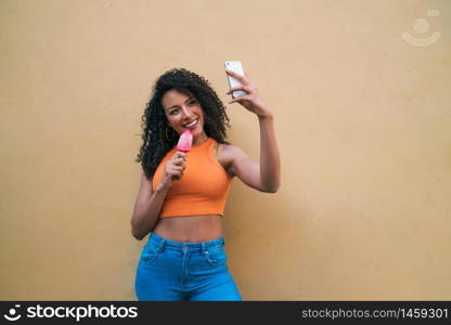 Portrait of afro woman taking selfies with her mophile phone while eating ice-cream. Technology and lifestyle concept.