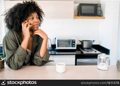 Portrait of afro woman talking on the phone with a cup of coffee at home. Communication concept.. Afro woman talking on the phone at home.