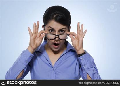 Portrait of amazed businesswoman looking over glasses against blue background