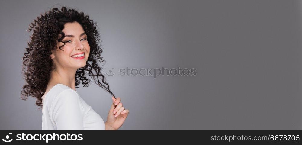 Portrait of amazing beautiful smiling woman with curly hair on gray background with copy space. Portrait of beautiful woman
