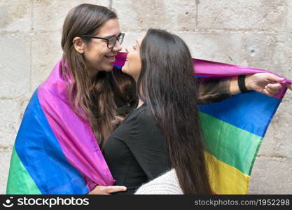 Portrait of an affectionate young lesbian couple hugging each other while standing together in front of a stone wall outside. High quality photo.. Portrait of an affectionate young lesbian couple hugging each other while standing together in front of a stone wall outside