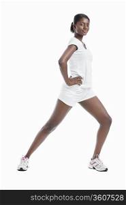 Portrait of an African American young woman stretching legs against white background
